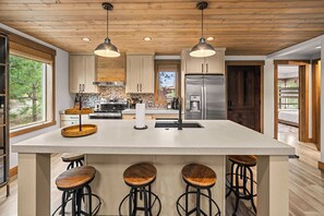 A modern kitchen with a large island, bar stools, wooden cabinets, and a stainless steel refrigerator. - Wilderness Club Park Cottage (Eureka)