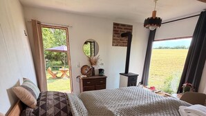 A bedroom with a large bed, a dresser, a mirror, and a view of a field through a window. - Tiny House with Sauna and Hot Tub: Nature, Relaxation, Peace, Wellness  (Schmölln)
