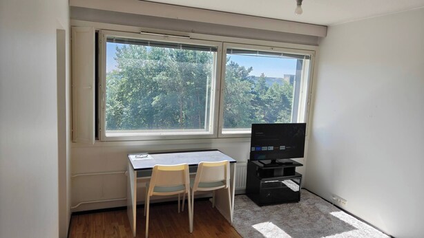 Una habitación con escritorio, dos sillas, televisor y ventana con vistas a árboles.