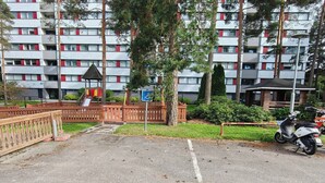 Un estacionamiento con área de juegos, señal de acceso para sillas de ruedas y un edificio de varios pisos con marcos de ventanas rojos.