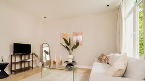 A living room with a sofa, a coffee table, a TV, a mirror, and two wall-mounted paintings. - New apartment in downtown Antwerp for 6 people (Antwerpen)
