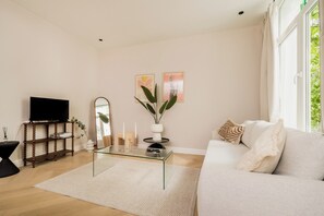 A living room with a sofa, a coffee table, a TV, a mirror, and two wall-mounted paintings. - New apartment in downtown Antwerp for 6 people (Antwerpen)