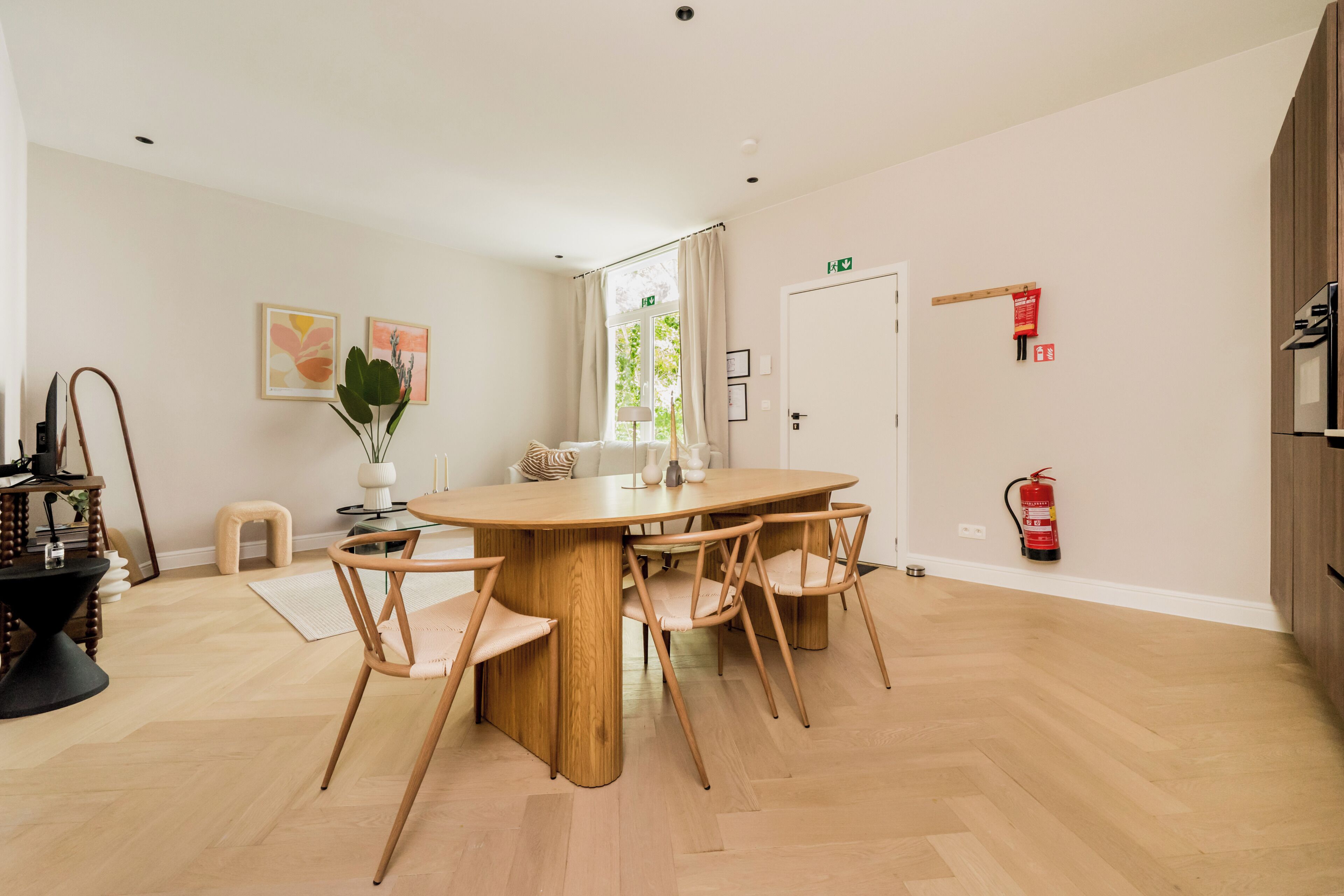 Un espace repas moderne avec une table ronde en bois et des chaises assorties, une petite table d’appoint avec un vase et des bougies, et une fenêtre avec des rideaux.