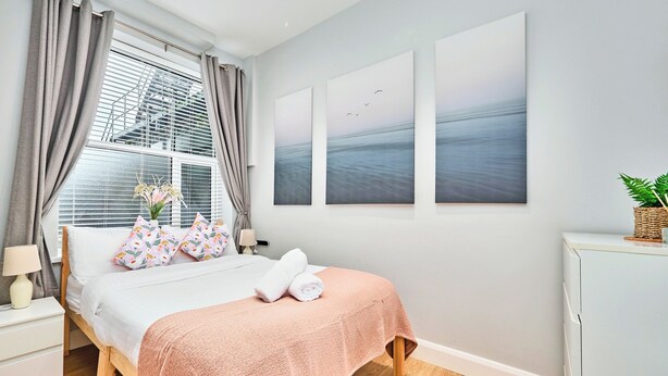 A bedroom with a bed, a nightstand, a lamp, a window with curtains, and wall art. - No.1 West Beach Apartments - UK52002 (Portrush)