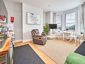 A modern living room with a sofa, a dining table, a TV, and a large window. - No.1 West Beach Apartments - UK52002 (Portrush)