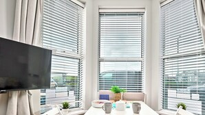 A room with a white table, two chairs, a television, and large windows with blinds. - No.1 West Beach Apartments - UK52002 (Portrush)