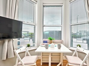 A room with a white table, two chairs, a television, and large windows with blinds. - No.1 West Beach Apartments - UK52002 (Portrush)
