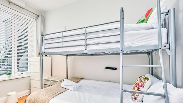 A bunk bed room with a window, a small table, and a trash bin. - No.3 West Beach Apartments - UK52003 (Portrush)