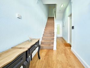 Ein Flur mit Holzboden, einer Treppe, einem Schreibtisch mit Lampe und einer Tür mit einer Nummer.'