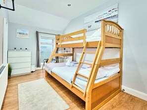 Un lit superposé avec une échelle, un bureau, une chaise, une petite table et une fenêtre avec des stores.