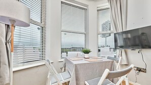 A modern room with a table, chairs, a TV, and large windows with blinds. - No.1 Dunluce Park Apartments - UK52007 (Portrush)