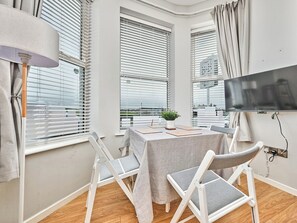 Ein modernes Zimmer mit Tisch, Stühlen, einem Fernseher und großen Fenstern mit Jalousien.