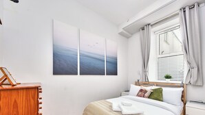 A bedroom with a bed, a bedside table, a nightstand, a window with curtains, and a wall-mounted picture. - No.1 Dunluce Park Apartments - UK52007 (Portrush)