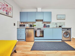 Eine kleine Küche mit blauen Schränken, einer Mikrowelle, einer Kaffeemaschine und einer Waschmaschine.