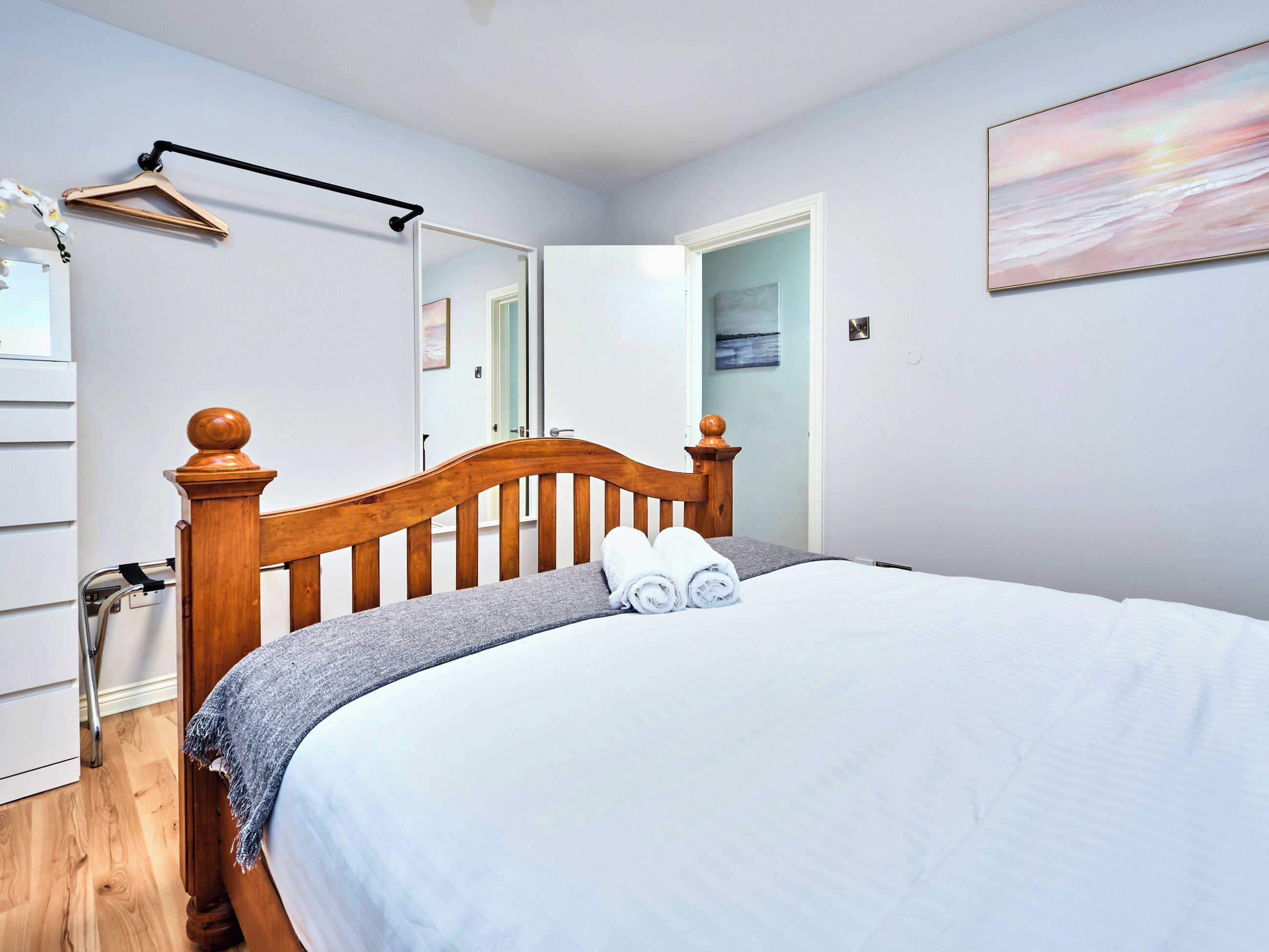 A neatly made bed with a wooden headboard, a grey blanket, and two rolled towels.
