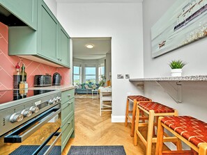 A kitchen with a stove, cabinets, and a dining area with stools. - No.3 Dunluce Apartments - UK52009 (Portrush)