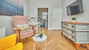 Een moderne woonkamer met een gestreepte fauteuil, een gele bank, een kleine witte tafel met een plant en een grijze kast met lades.