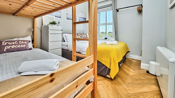 Een slaapkamer met een stapelbed, een bureau, een stoel, een raam met uitzicht en een radiator.