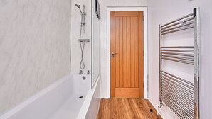 Ein Badezimmer mit einer Badewanne, einer Holztür und einem Handtuchhalter.