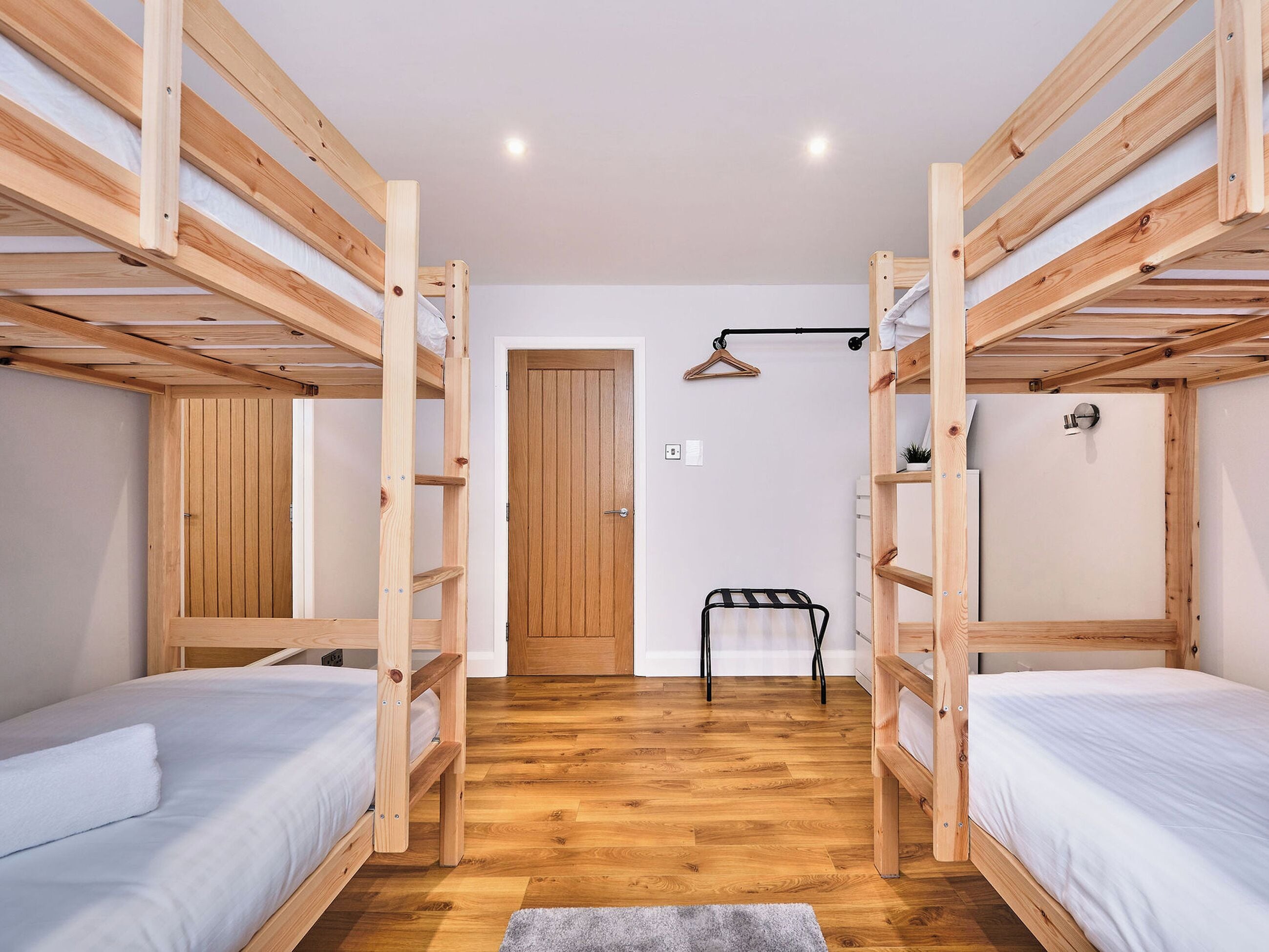 Une pièce avec deux lits superposés, une porte en bois, une petite table et un porte-vêtements suspendu.