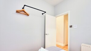 Een slaapkamer met een bed, een houten kapstok, een witte deur en een radiator.
