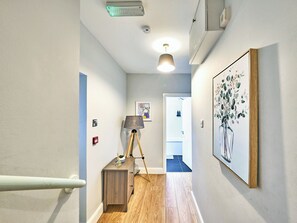 A hallway with a wooden floor, a lamp, a painting, and a door leading to another room. - No.2 Dunluce Green Apartments - UK52015 (Portrush)