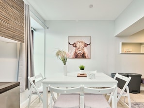 A modern dining area with a white table, four chairs, a vase with flowers, a framed picture of a bull, and a small plant. - No.2 Dunluce Green Apartments - UK52015 (Portrush)