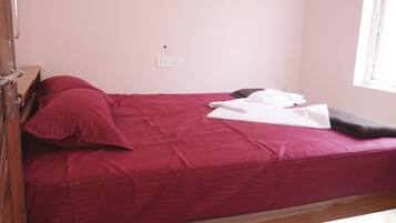 Una cama individual con una colcha roja, una almohada blanca y una manta blanca doblada.