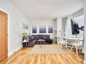 Ein modernes Wohnzimmer mit einer Couch, einem Couchtisch, einem Fernseher und einem Schreibtisch mit Stühlen.