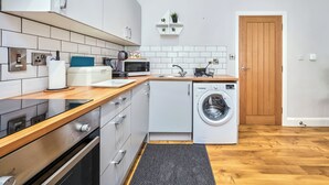 A modern kitchen with white cabinets, a microwave, a kettle, and a washing machine. - No.2 Princess Red Apartments - UK52041 (Portrush)