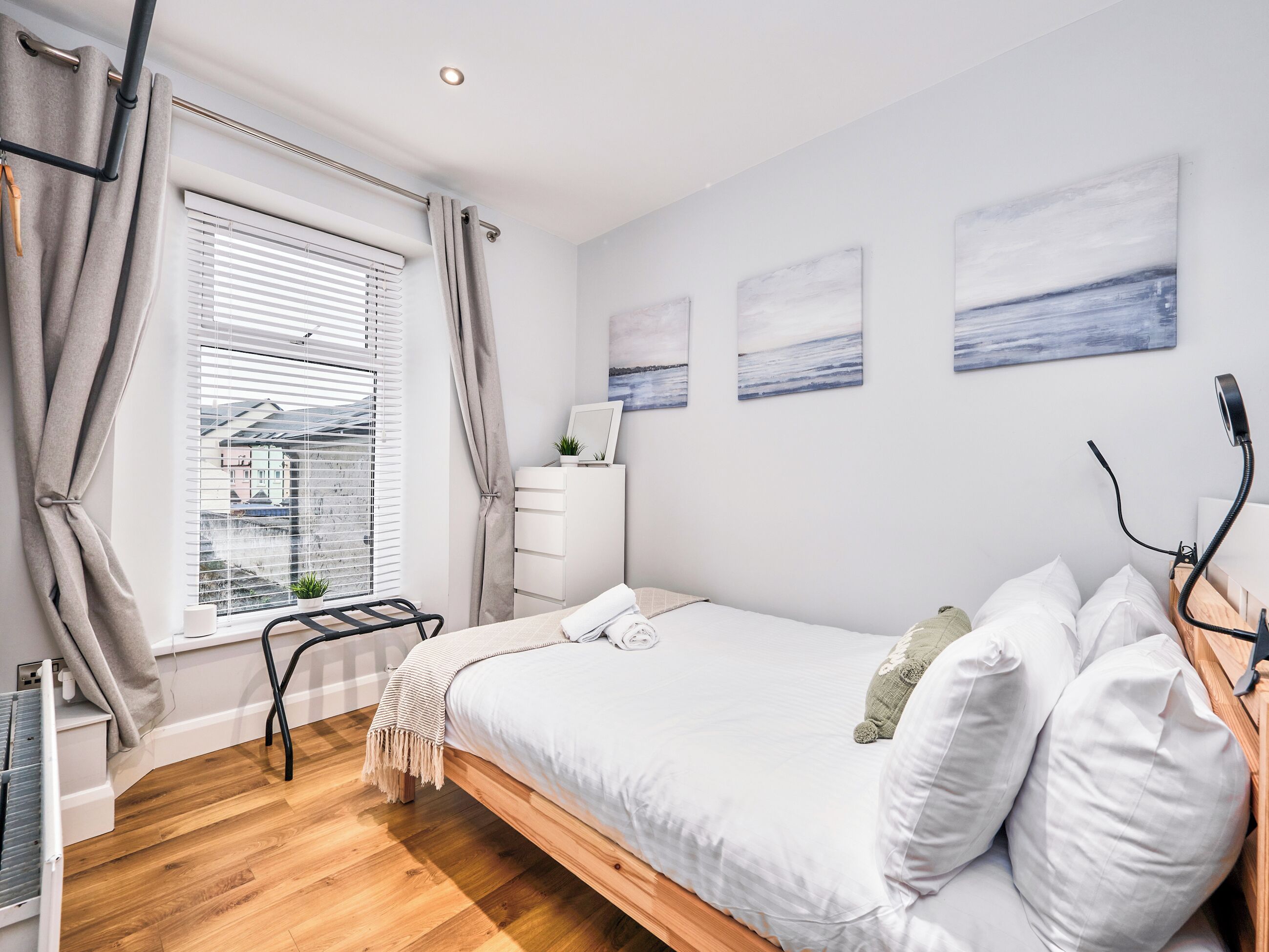 A bedroom with a bed, a dresser, a window with curtains, and wall art.