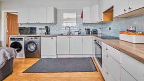 A compact kitchen with a washing machine, dishwasher, microwave, and a coffee maker. - No.6 Dunluce Park Apartments - UK52047 (Portrush)