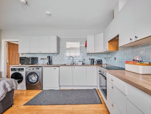 A compact kitchen with a washing machine, dishwasher, microwave, and a coffee maker. - No.6 Dunluce Park Apartments - UK52047 (Portrush)