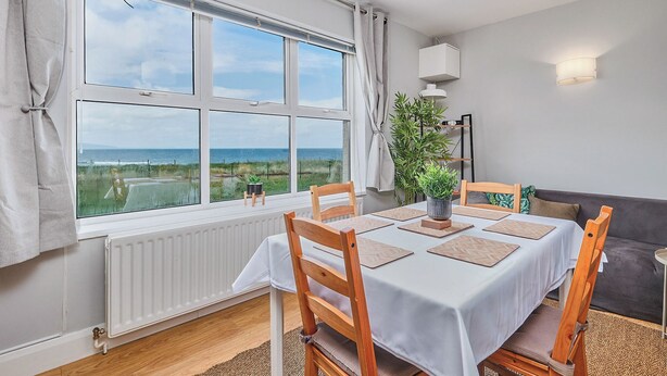 A dining area with a table set for four, large windows with a view of the sea, a radiator, and a plant on the windowsill. - No.6 Dunluce Park Apartments - UK52047 (Portrush)