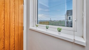 A room with a wooden door, a window with a view of a distant building, and a shelf with small potted plants. - No.6 Dunluce Park Apartments - UK52047 (Portrush)