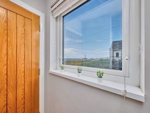 A room with a wooden door, a window with a view of a distant building, and a shelf with small potted plants. - No.6 Dunluce Park Apartments - UK52047 (Portrush)