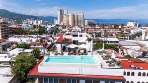 A rooftop pool with lounge chairs and umbrellas, surrounded by buildings and a mountainous backdrop. - Deluxe 2BD corner unit & Rooftop Pool in Versalles 2BD Condo for rent in Versall (Puerto Vallarta)