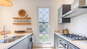 A modern kitchen with a gas stove, stainless steel sink, and a decorative window with a geometric pattern. - Deluxe 2BD corner unit & Rooftop Pool in Versalles 2BD Condo for rent in Versall (Puerto Vallarta)