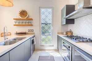 Eine moderne Küche mit Gaskochfeld, Edelstahlspüle und einem dekorativen Fenster mit geometrischem Muster.