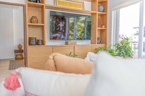 Una sala de estar moderna con un televisor de pantalla plana grande montado en una pared de madera, un sofá cómodo con cojines y vistas al exterior con vegetación.