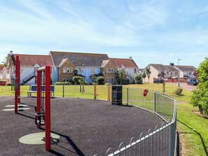 A playground with a swing set and a slide, surrounded by a metal fence.