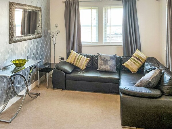A living room with a black leather sofa, a glass coffee table, a mirror, and a vase with flowers.
