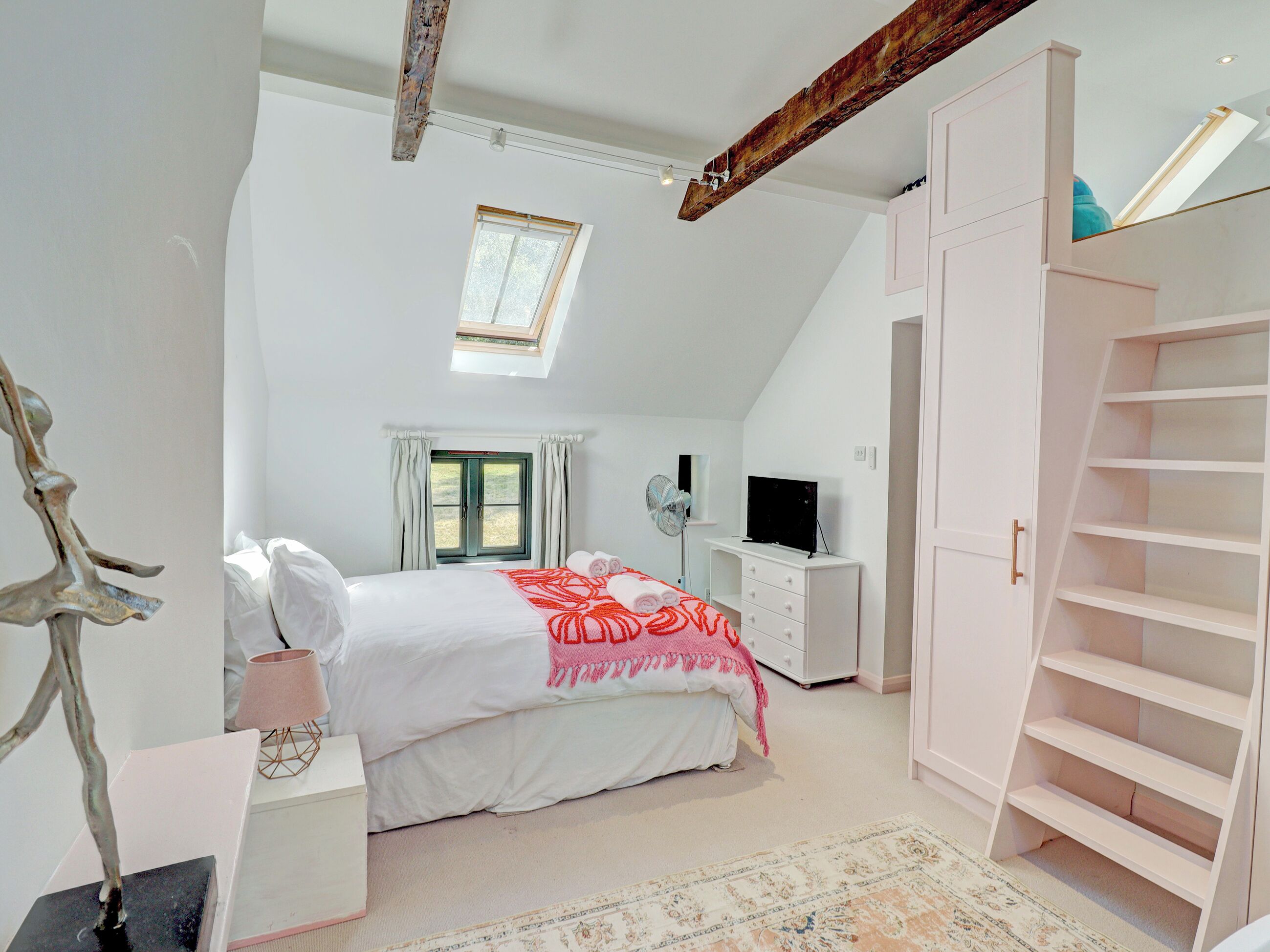 A bedroom with a bed, a desk, a TV, a wardrobe, and a skylight.