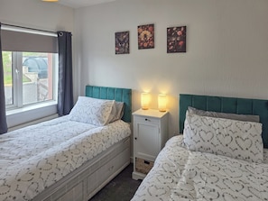 Ein Schlafzimmer mit zwei Betten, einem Nachttisch und einem Fenster mit Vorhängen.
