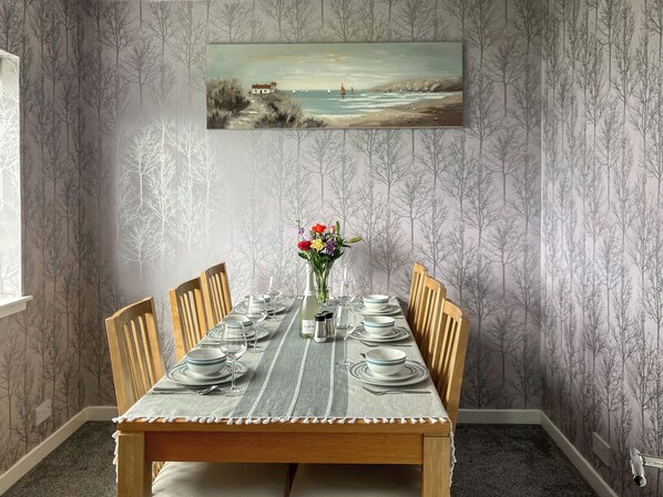 A dining room with a table set for four, chairs, a painting on the wall, and a window.