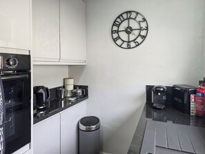 A kitchen with a wall clock, a coffee maker, a toaster, and a trash bin.