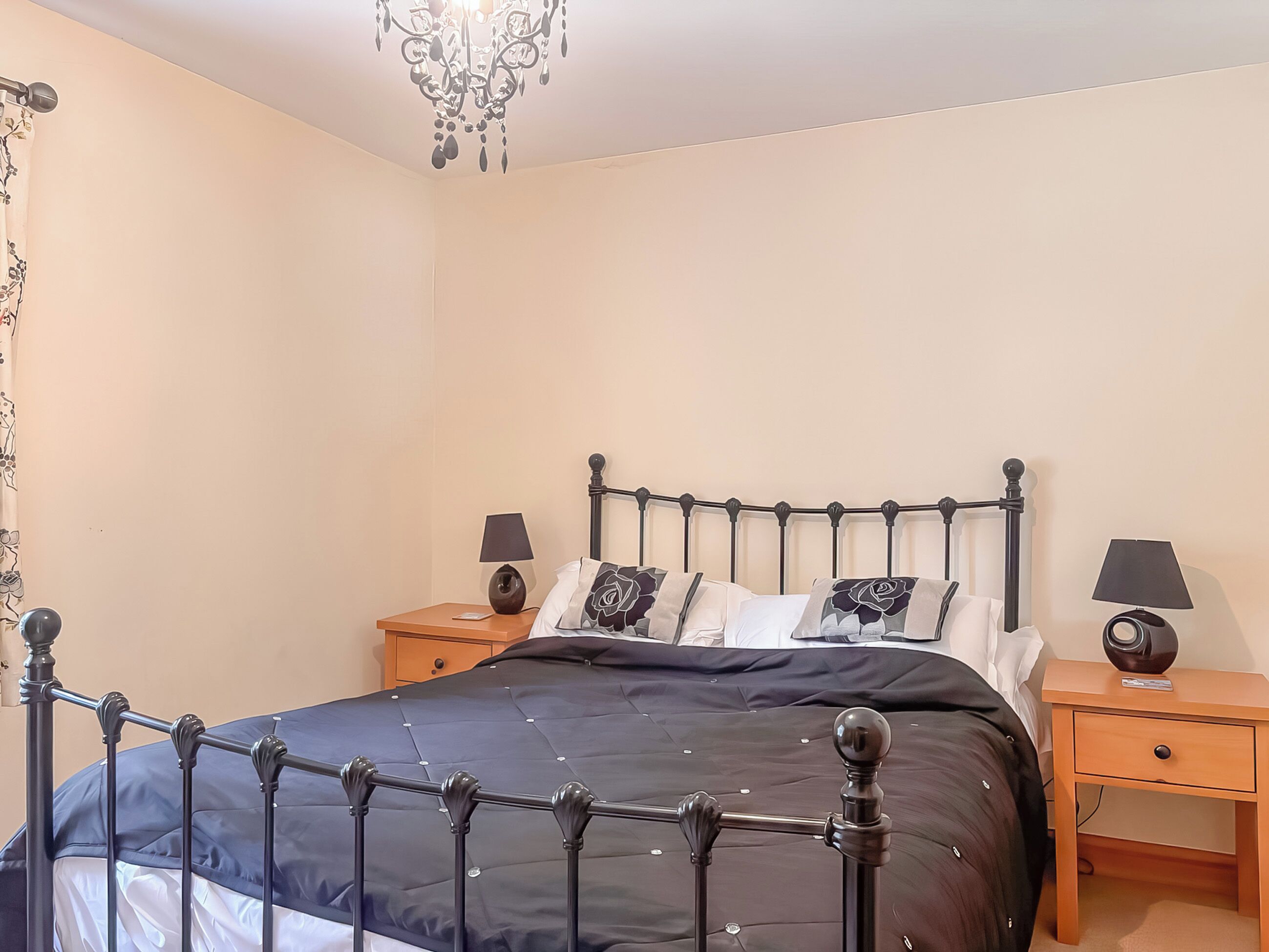 A bedroom with a four-poster bed, two bedside tables, a chandelier, and a window with curtains.