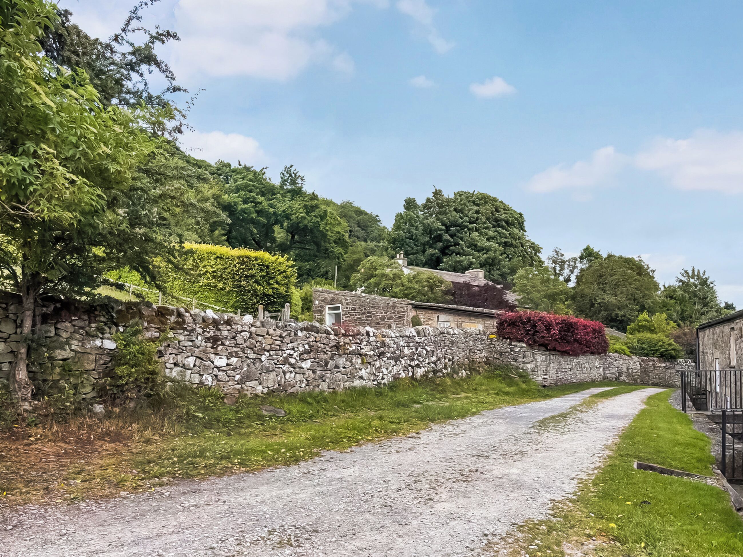 A rural road with stone walls and greenery.