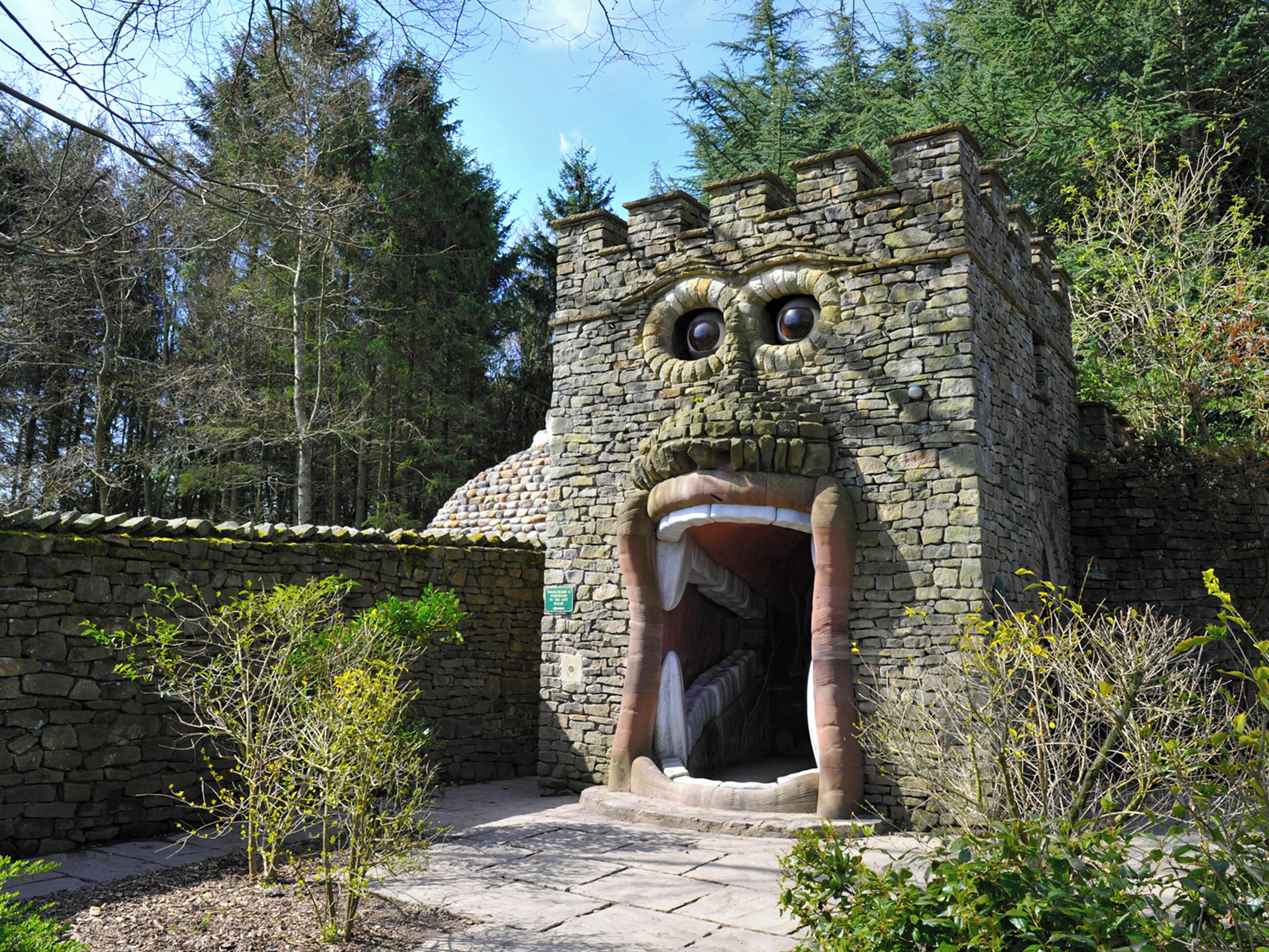 Um edifício de pedra com uma grande face caricata esculpida na fachada, rodeado de árvores.