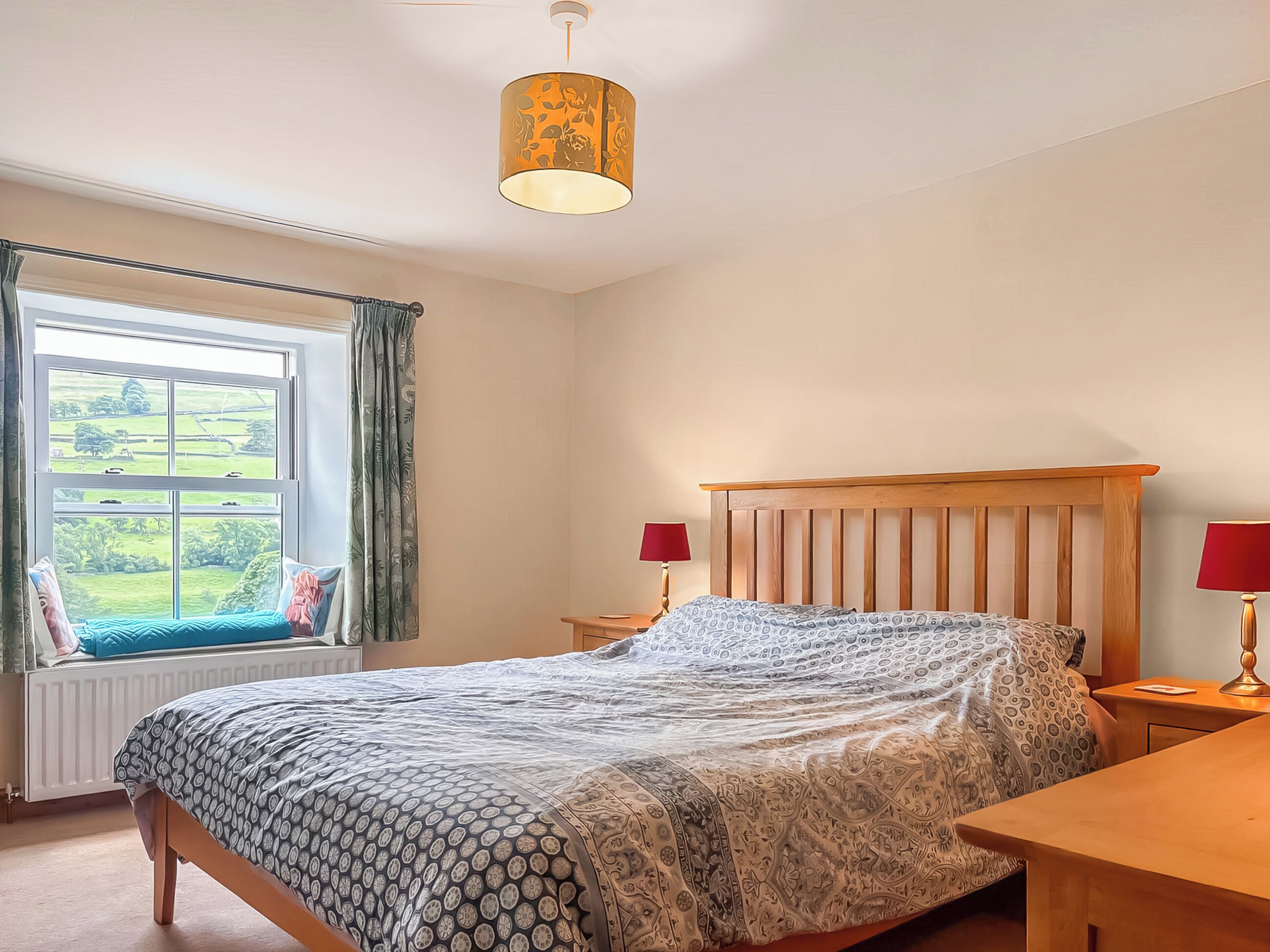 Une chambre à coucher avec un lit, deux tables de chevet, une fenêtre avec des rideaux et une lampe suspendue.